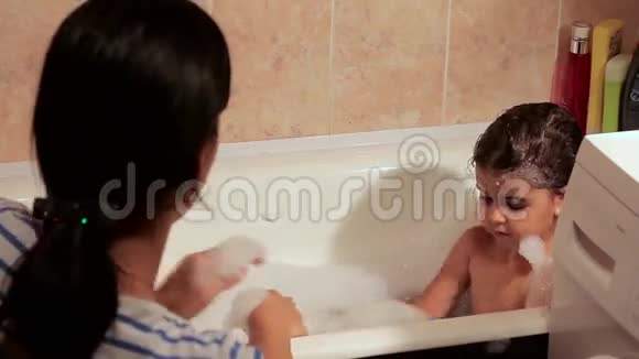 美丽的女孩沐浴在泡沫中她笑了和她妈妈玩得很开心四面八方飞起的泡沫视频的预览图