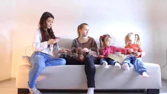 两个年轻的母亲和两个小女儿坐在客厅的沙发上视频的预览图