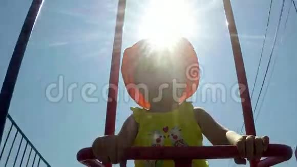 在蓝天上太阳背景下秋千上的一个小孩子的肖像画视频的预览图