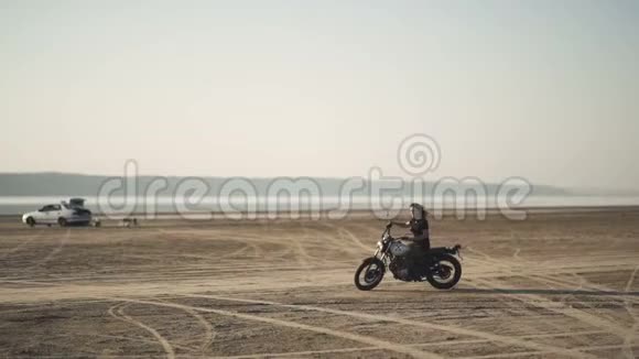 美丽的年轻女子骑着一辆古老的咖啡馆赛车摩托车做着一个诡计在日落或日出的沙漠里女自行车手视频的预览图