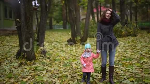 一位美丽的年轻女子带着一个孩子在秋天的公园里散步一个快乐的母亲和一个小女儿正在走视频的预览图
