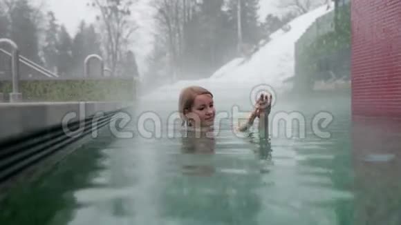 下雪时在室外游泳池放松的美女视频的预览图