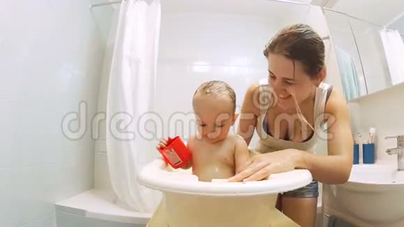美丽慈爱的母亲亲吻她的小儿子在塑料浴缸里洗澡视频的预览图