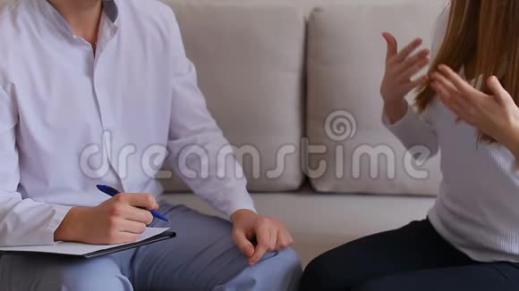 女人来看医生听和写一男一女坐在灰色沙发上的医疗办公室视频的预览图