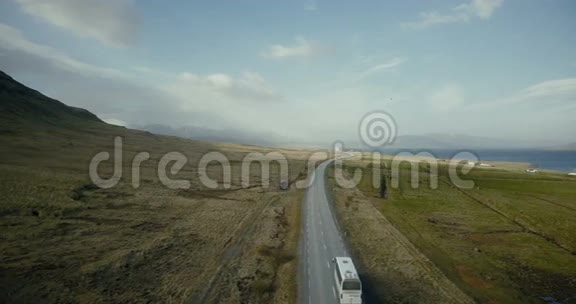 鸟瞰山道汽车在靠近大海的高速公路上穿过绿色的田野视频的预览图