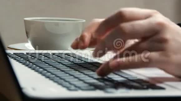 女性手在笔记本电脑的键盘上打字拿着茶杯喝茶或咖啡视频的预览图