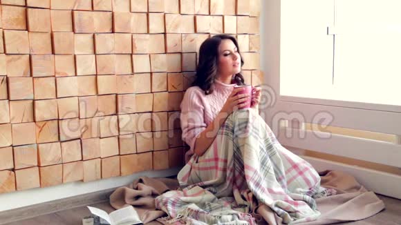 美丽的女人喝着咖啡或茶在家看着窗户视频的预览图