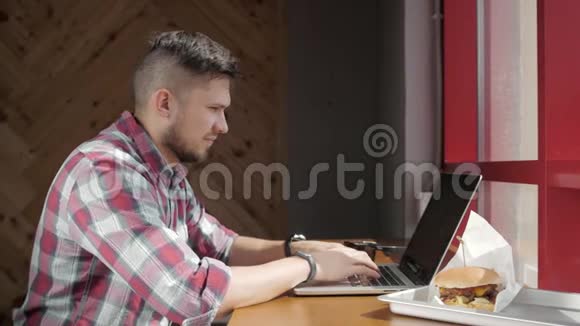 忙碌的年轻商人坐在快餐店内部的酒杯和汉堡包的画像视频的预览图
