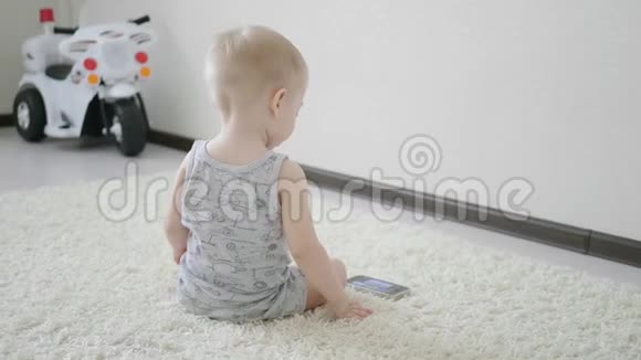 小男孩在家里的地板上看智能手机上的卡通生活方式视频的预览图