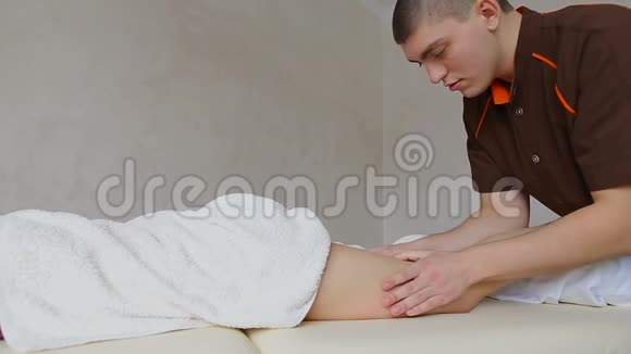 专业按摩师揉捏女病人的腿她躺在明亮的办公室沙发上视频的预览图