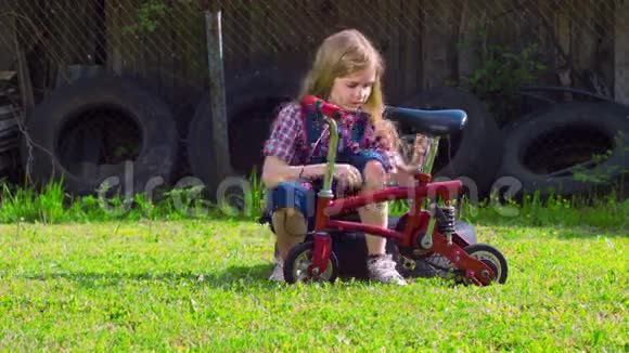 女孩在阳光明媚的绿色草地上修理自行车视频的预览图