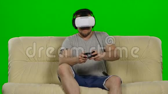 戴虚拟现实护目镜的人摄影棚白色沙发绿色屏幕视频的预览图