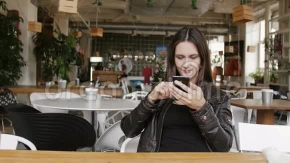 时尚的年轻女性使用智能手机上网坐在现代咖啡馆的桌子旁微笑4K视频的预览图