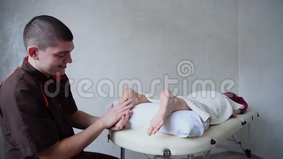 男医生给躺在明亮医疗沙龙沙发上的年轻女孩按摩脚视频的预览图