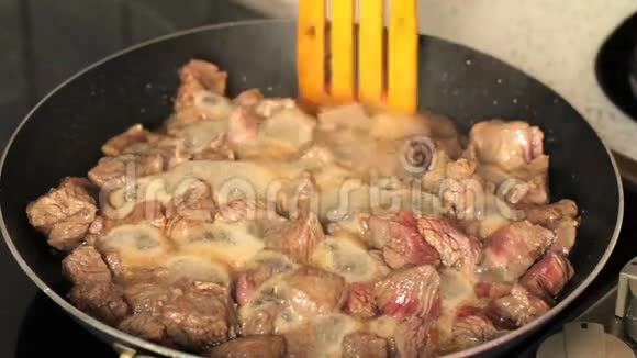 在煎锅里煎肉煎锅里的肉与木铲混合肉在自己的果汁中沸腾视频的预览图