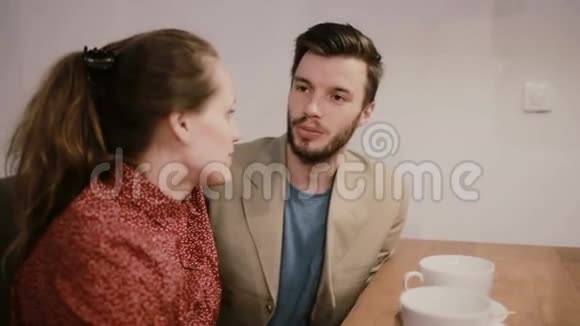 一对相爱的夫妇坐在桌子上的沙发上上面有空咖啡杯他们在说话和微笑视频的预览图