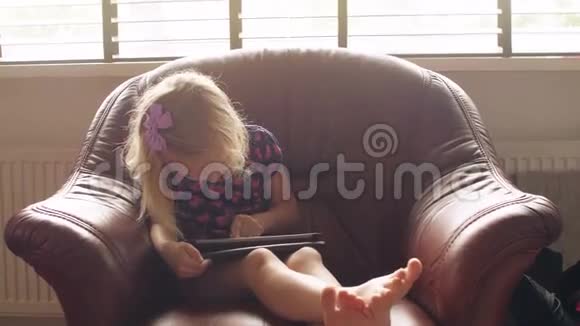 一个可爱的金发小女孩穿着所有粉红色的衣服坐在柴兰德玩平板电脑游戏4k视频的预览图