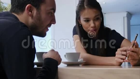 在咖啡馆里微笑的年轻女子向男性朋友展示了她的手机视频的预览图