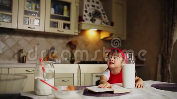 女儿穿着红色围裙在厨房里在笔记本上读食谱蛋糕视频的预览图