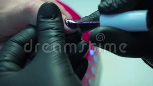 专业的美甲师在美容院用黑色手套修指甲深紫色漂亮的粉红色指甲近距离拍摄视频的预览图