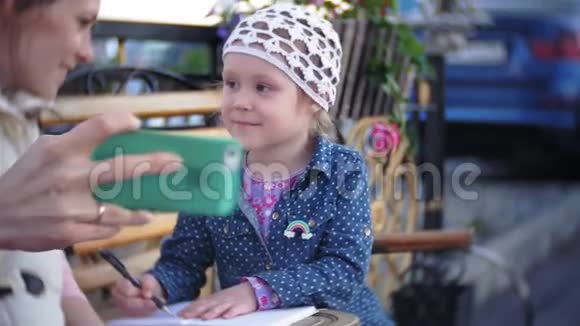 小漂亮女孩和她的母亲坐在公园的长凳上手里拿着她的笔记本她穿着一件外套她是视频的预览图