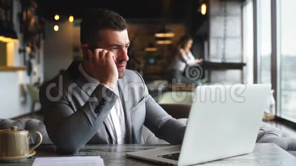 年轻的商人用手提电脑和电话聊天在咖啡馆的桌子上视频的预览图