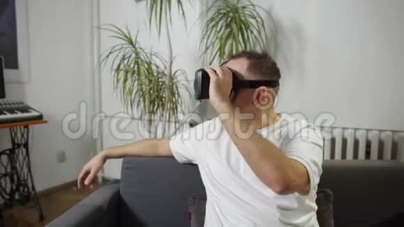 穿白色衬衫的男人在沙发上享受虚拟现实视频的预览图