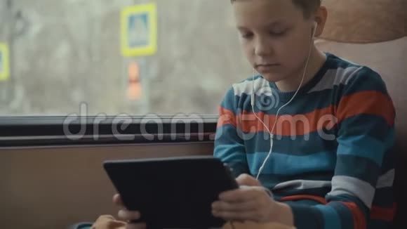 一个小男孩乘公共汽车穿过城市在他的电脑平板电脑上使用社交网络的特写镜头视频的预览图