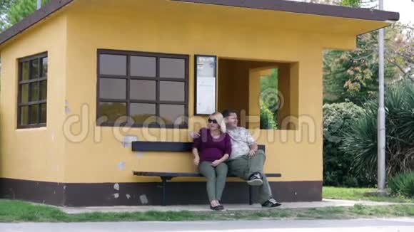 一对夫妇坐在橙色房子前面的长凳上视频的预览图