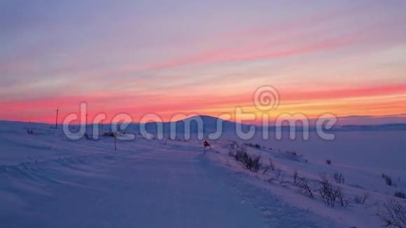 在猩红的日落背景下两辆带着侧车的摩托车沿着远离极地圈的白雪覆盖的道路行驶视频的预览图