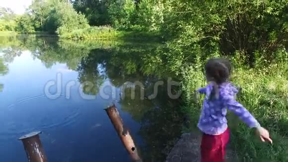 女孩子在池塘的水里扔小石头这个池塘位于老的杂草丛生的公园里视频的预览图
