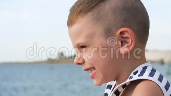 天空和大海背景上穿着水手条纹衬衫的快乐小男孩视频的预览图