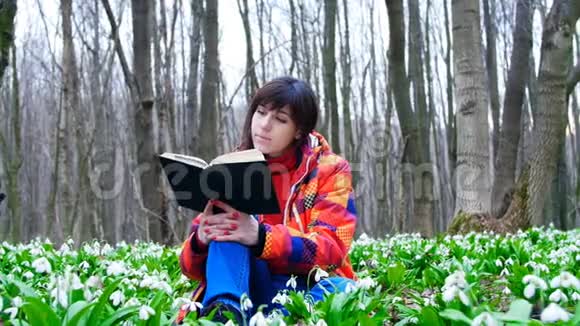 一个漂亮聪明的女孩正在春天的森林里读一本有趣的书里面满是朵朵的雪花视频的预览图