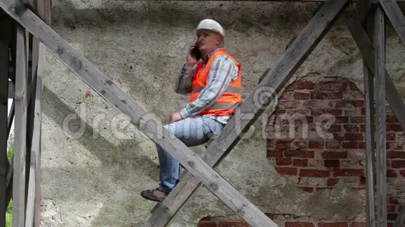 建筑工人坐在木脚手架上打电话视频的预览图
