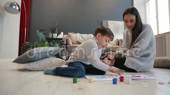 母亲带着一个孩子在他的房子的白色内部被打开油漆罐坐在地板上蘸着你的水视频的预览图