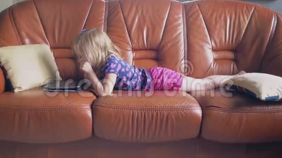 一个可爱的金发小女孩穿着所有粉红色的侧视图躺在沙发上在平板电脑上玩游戏4k视频的预览图
