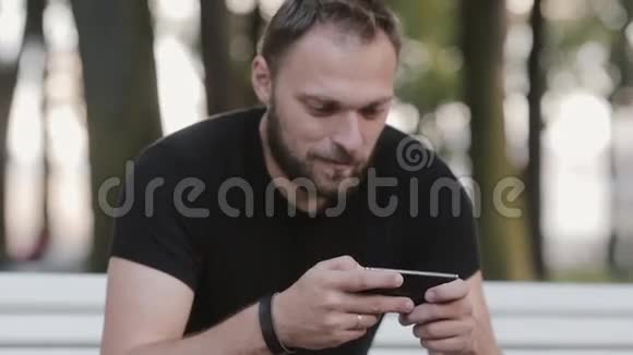 在公园里坐在长凳上用智能手机描绘一个迷人的年轻人视频的预览图