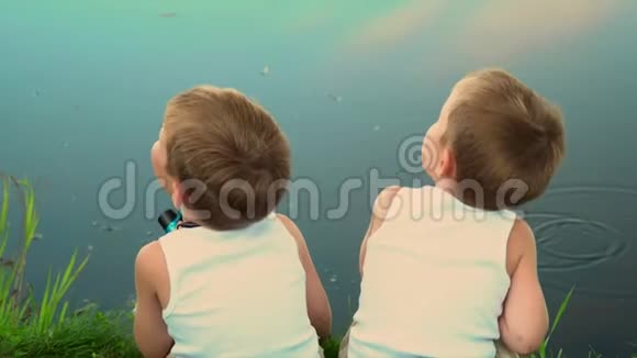 两兄弟在露天捕鱼两个钓鱼的小渔夫戴光帽的孩子们坐在池塘的岸边视频的预览图