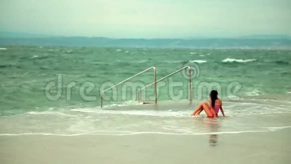 女孩坐在水泥海岸上观察着沉重的海洋视频的预览图