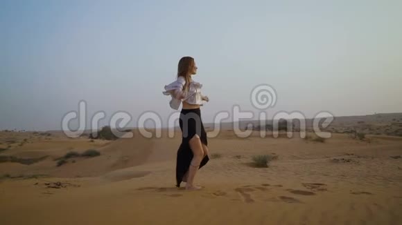 漂亮的女孩在沙漠里跳舞美丽的女人在日落时跳舞慢动作视频的预览图