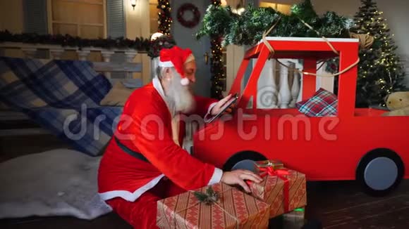 圣诞老人在平板电脑上检查礼物清单并把礼物放进车里视频的预览图