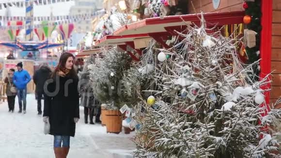 俄罗斯莫斯科的圣诞市场上一位年轻漂亮的女士在下雪的天气里散步并检查纪念品视频的预览图