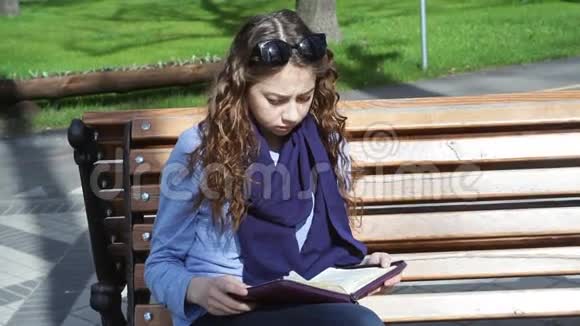 年轻女子坐在公园的长凳上看书视频的预览图