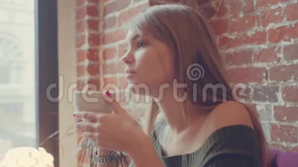 年轻漂亮的女人在咖啡馆里喝热咖啡快乐放松的女孩享受一杯温暖的热气腾腾的饮料视频的预览图