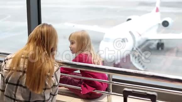 母亲和女儿正透过窗户看一架飞机飞机来到了登机门视频的预览图