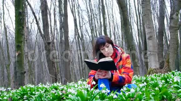 一个漂亮聪明的女孩正在春天的森林里读一本有趣的书里面满是朵朵的雪花视频的预览图