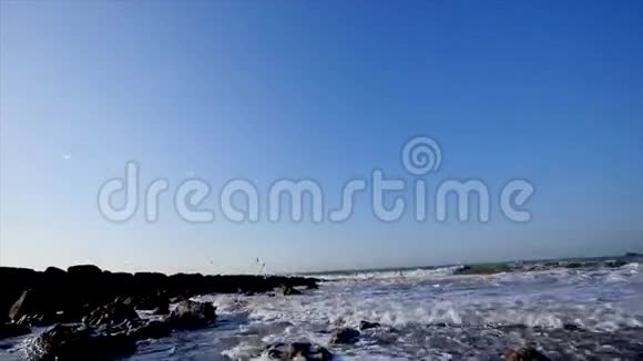 在蓝天背景下海浪和在岩石和山脉附近飞翔的海鸥视频的预览图