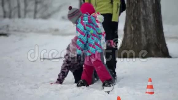当一家人走在大型滑雪板上时孩子们笑着玩着一个接一个地摔倒视频的预览图