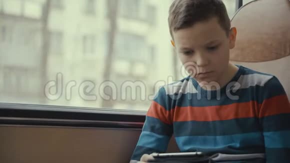 一个小男孩乘公共汽车穿过城市在他的电脑平板电脑上使用社交网络的特写镜头视频的预览图