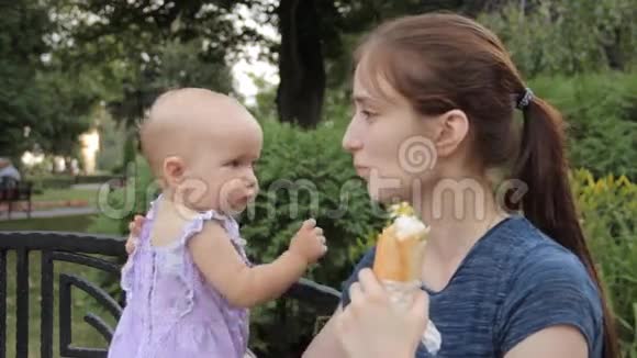 一个年轻的女孩抱着一个女婴一只手坐在公园的长凳上视频的预览图